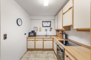 Een kleine keuken met een magnetron, broodrooster, waterkoker en een klok aan de muur.