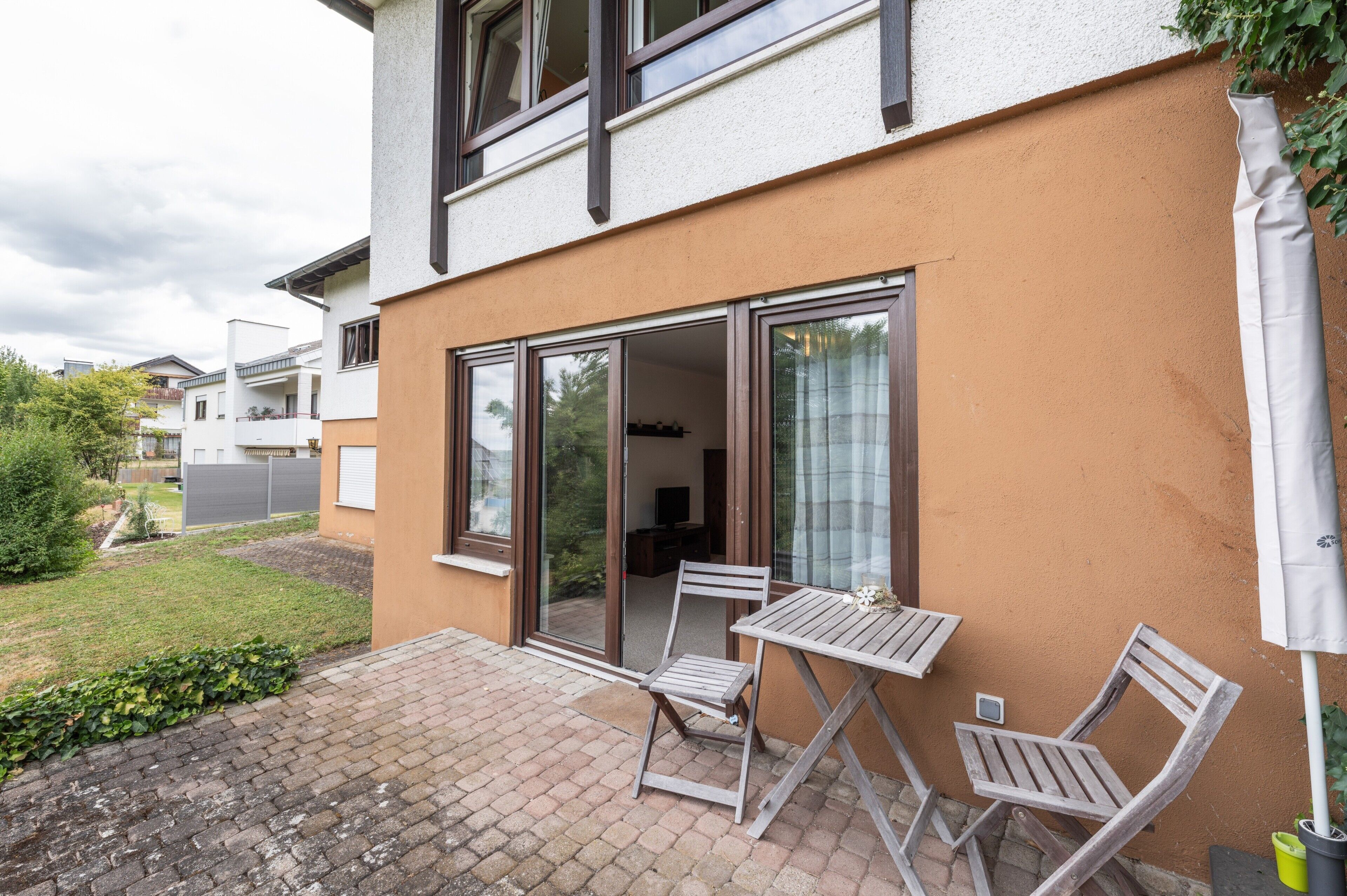 Un immeuble résidentiel doté d’un patio comprenant une table et des chaises, une porte-fenêtre coulissante et un petit jardin.