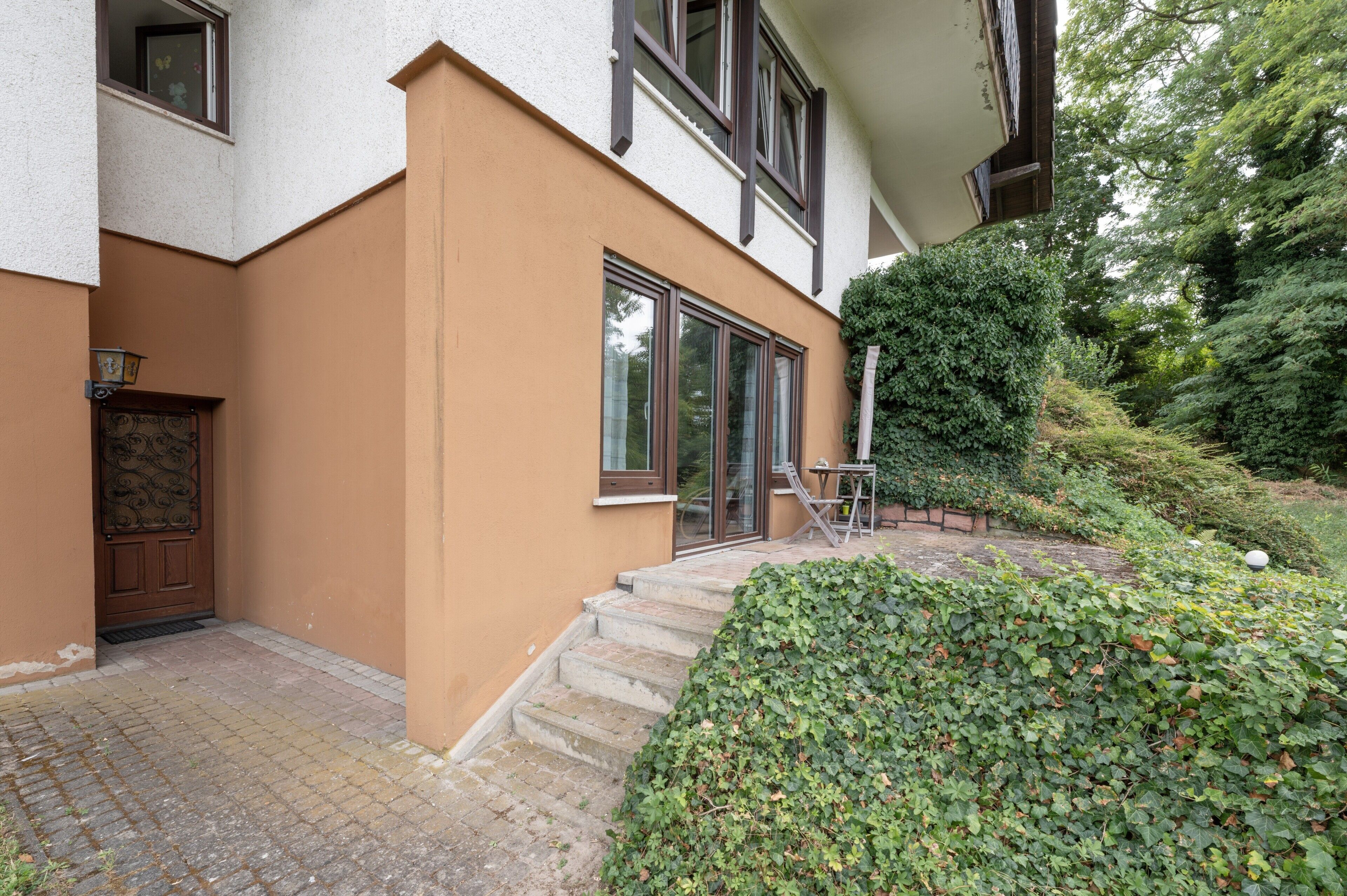 A building with a brown exterior, a wooden door, and a set of stairs leading to a glass door.