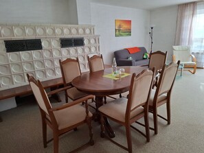 A dining area with a round table, six chairs, a decorative wall panel, a sofa, and a floor lamp.