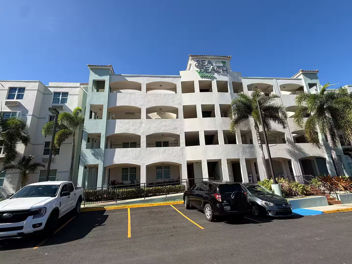 Un hotel de varios pisos con un atrio central, estacionamiento y palmeras.