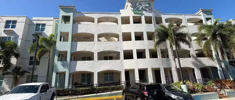 Un hotel de varios pisos con un atrio central, estacionamiento y palmeras.
