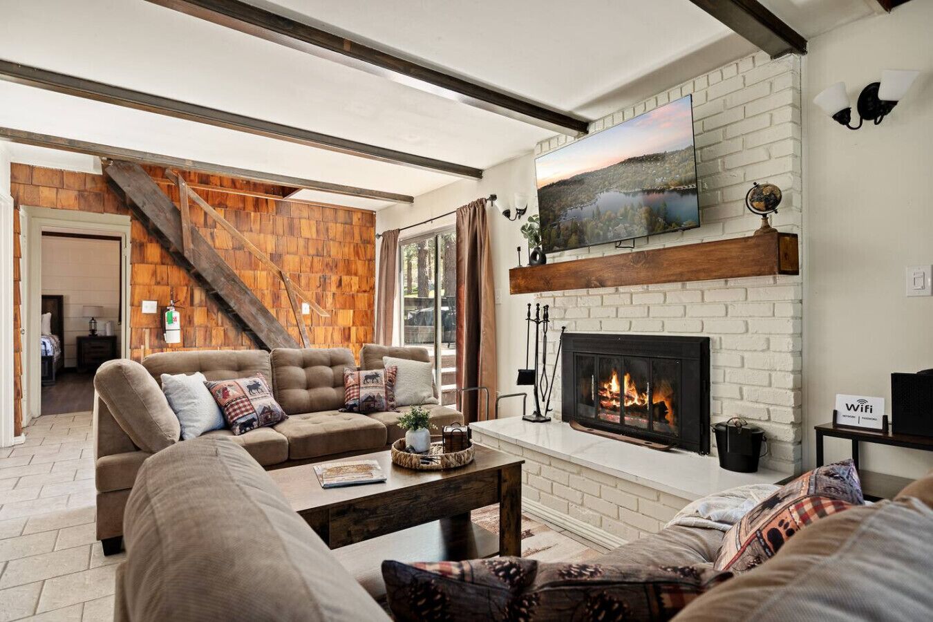 Een woonkamer met een open haard, een trap en een aan de muur bevestigde televisie.