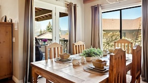Un espace repas comprenant une table en bois, des chaises, un lustre et une vue sur l’ext érieur.