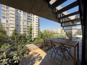 A balcony with a wooden table and chairs, overlooking a residential area with multiple apartment buildings and greenery. - Premium Duplex with Private Pool (Providencia)