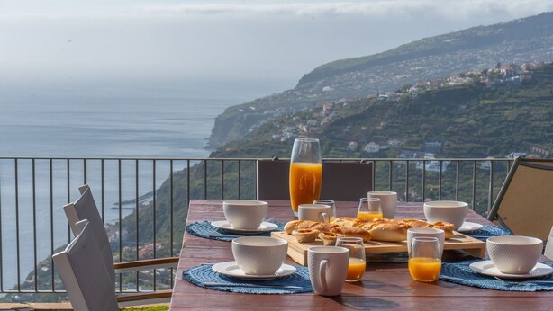 Ein Tisch mit Frühstücksangeboten und einem Glas Orangensaft mit Blick auf eine Küstenlandschaft.