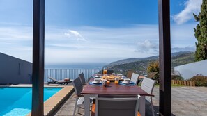 A dining table with chairs and a view of the ocean. - Duskline Villa by LovelyStay (Arco Da Calheta)