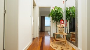 A hallway with a wooden floor, a mirror, a wicker vase with flowers, and a fire extinguisher. - Duskline Villa by LovelyStay (Arco Da Calheta)