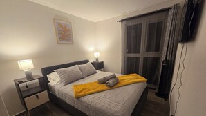Una cama bien hecha con almohadas, una lámpara de noche y una manta amarilla.