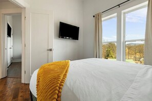 Quarto com cama, televisão na parede e janela com cortinas.