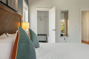 Ein Hotelzimmer mit Bett, Nachttischlampe, Spiegel und Blick ins Bad.