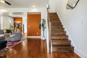 Eine Treppe führt zu einer oberen Etage, ein Essbereich mit Stühlen und ein Wohnzimmer mit Sofa und Teppich.