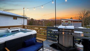 Una terrazza con idromassaggio, barbecue e luci decorative, con il sole al tramonto sullo sfondo.