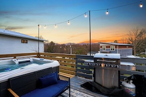 Eine Terrasse mit Whirlpool, Grill und Lichterkette vor einem Sonnenuntergang.