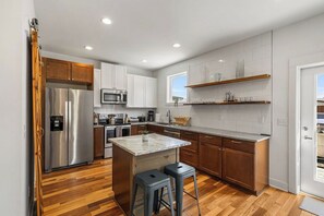 A modern kitchen with stainless steel appliances, wooden cabinets, and a marble island. - Blue Ridge House with Hot Tub - 204 (Asheville)