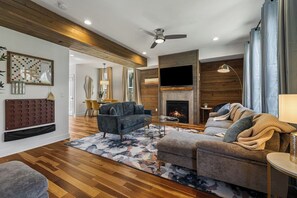 Ein modernes Wohnzimmer mit Kamin, Deckenventilator und flachbildschirm-Fernseher an der Wand.