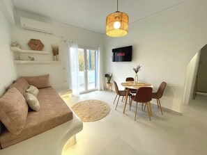 Un salon moderne comprenant un canapé, une table à manger, des chaises, un téléviseur et une grande fenêtre.