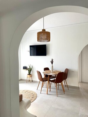 Un coin repas avec une table ronde, des chaises, un luminaire suspendu, un téléviseur à écran plat et une plante en pot.