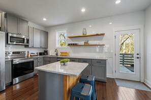 Een moderne keuken met grijze kastjes, een centraal eiland, blauwe krukken en een houten plank.