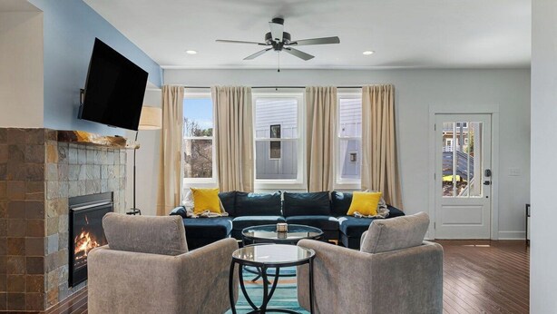 Un salon avec une cheminée, un canapé, deux fauteuils, une table basse et un ventilateur de plafond.