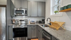 Une cuisine moderne dotée d’appareils électroménagers en acier inoxydable, de meubles gris, d’un plan de travail en granit et d’une fenêtre offrant une vue agréable.