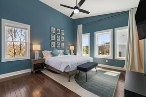 Une chambre à coucher avec un lit, des tables de chevet, un ventilateur de plafond et de grandes fenêtres.