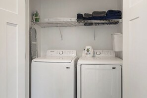 Een wasserette met twee witte voorladers, een metalen droogrek erboven en een witte deur.