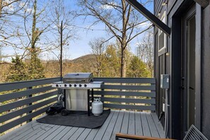A deck with a barbecue grill, a gas tank, and a metal grate.
