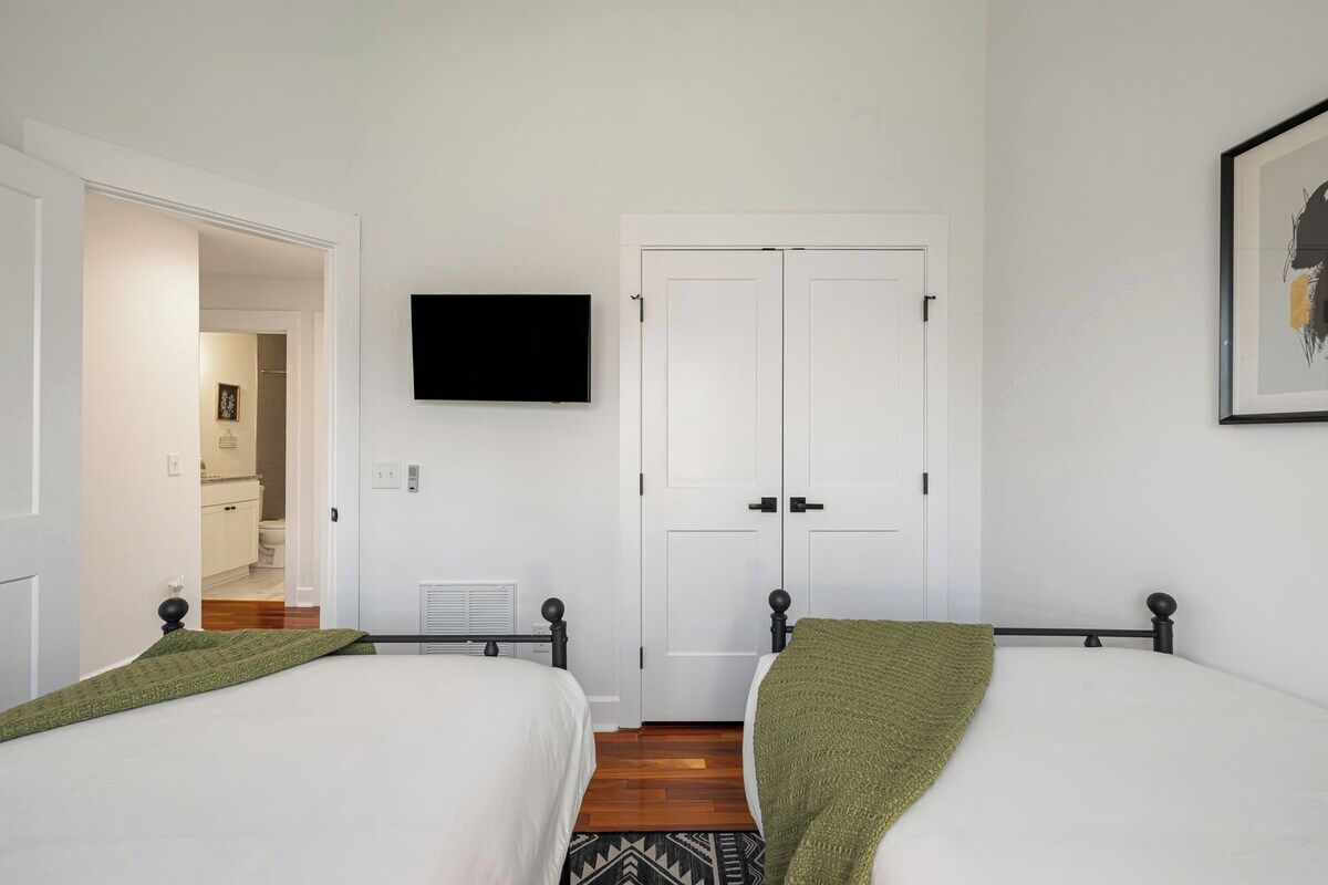 A bedroom with two beds, a television mounted on the wall, and a door leading to a bathroom.