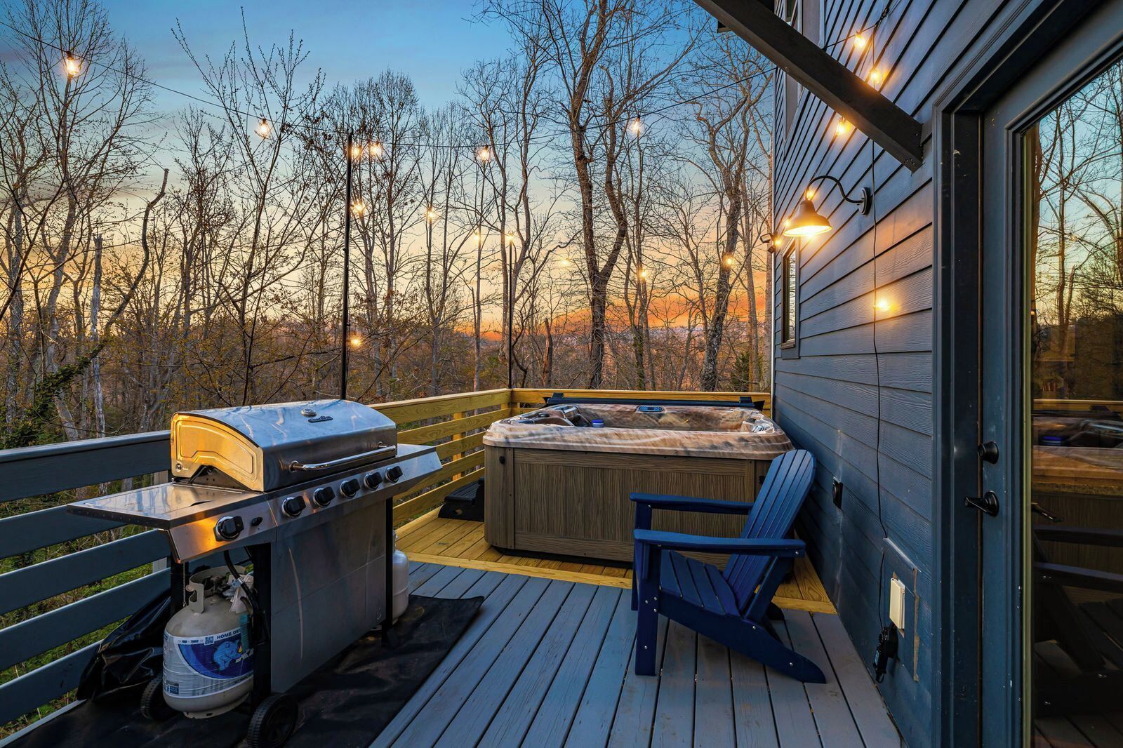 A deck with a grill, hot tub, and seating area overlooking a forested landscape.