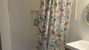 Ein Badezimmer mit einer Badewanne, einer Duschvorhang mit Tiermotiven, einem weißen Waschbecken und einem Holzkabinet.