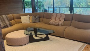 Ein modernes Wohnzimmer mit einem Ecksofa, einem Glastisch und einem gemusterten Teppich.