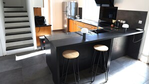 Une cuisine moderne dotée d’un îlot central, de tabourets de bar, d’un réfrigérateur en acier inoxydable et d’un four encastré.