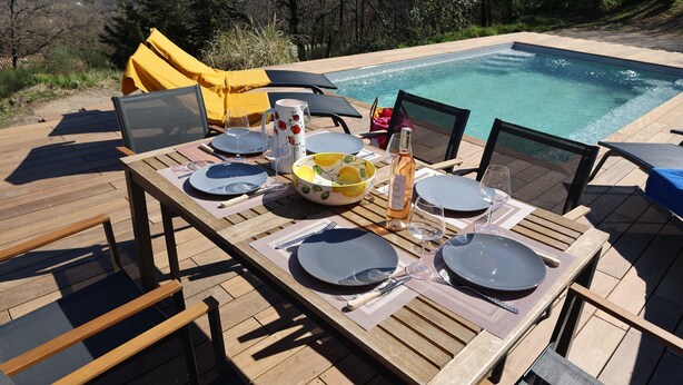 Une terrasse en bois avec une table dressée pour le repas, donnant sur une piscine et un paysage montagneux.