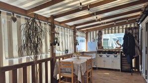 Habitación con estructura de madera, una mesa de comedor, sillas, una planta colgante y una zona de cocina con armarios y un refrigerador.