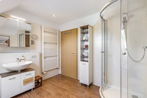 A modern bathroom with a sink, mirror, towel rack, shower, and storage cabinet.