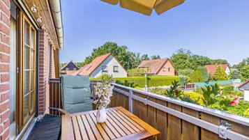 A wooden deck with a table and a chair, a potted plant, and a view of houses and greenery in the background.