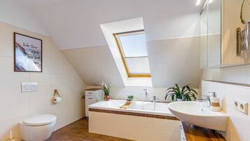 A modern bathroom with a skylight, a large bathtub, and a sink.