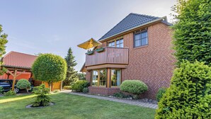 Une maison à deux étages, construite en briques, avec un balcon, un petit jardin et un toit recouvert de tuiles rouges.