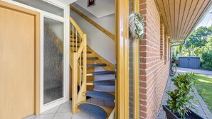 Un escalier en bois mène à une pièce dotée d’une porte en verre, d’un mur en briques et d’une plante en pot.