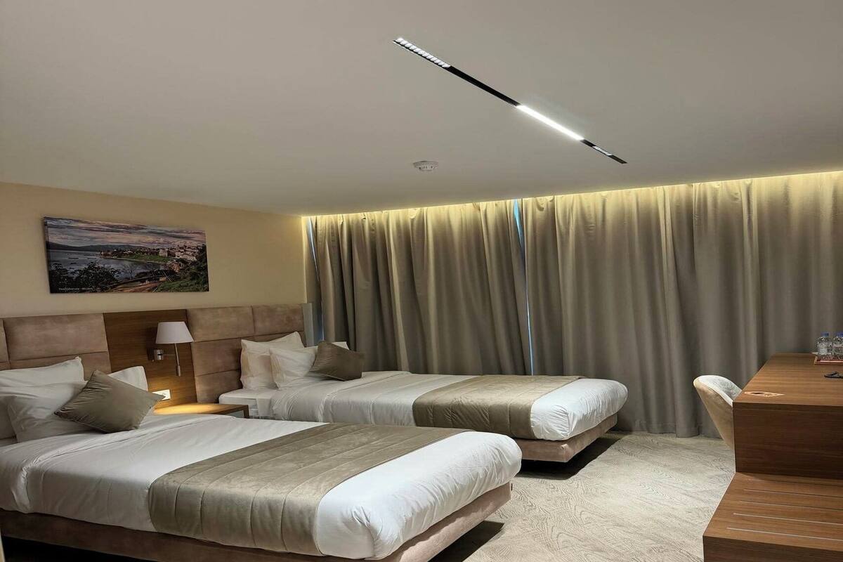 A hotel room with two beds, a desk, a lamp, and a painting on the wall.