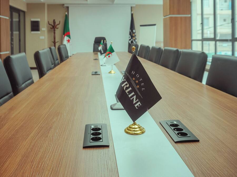 A conference room with a long table, flags, and a 'HOTEL KRINGE' sign.