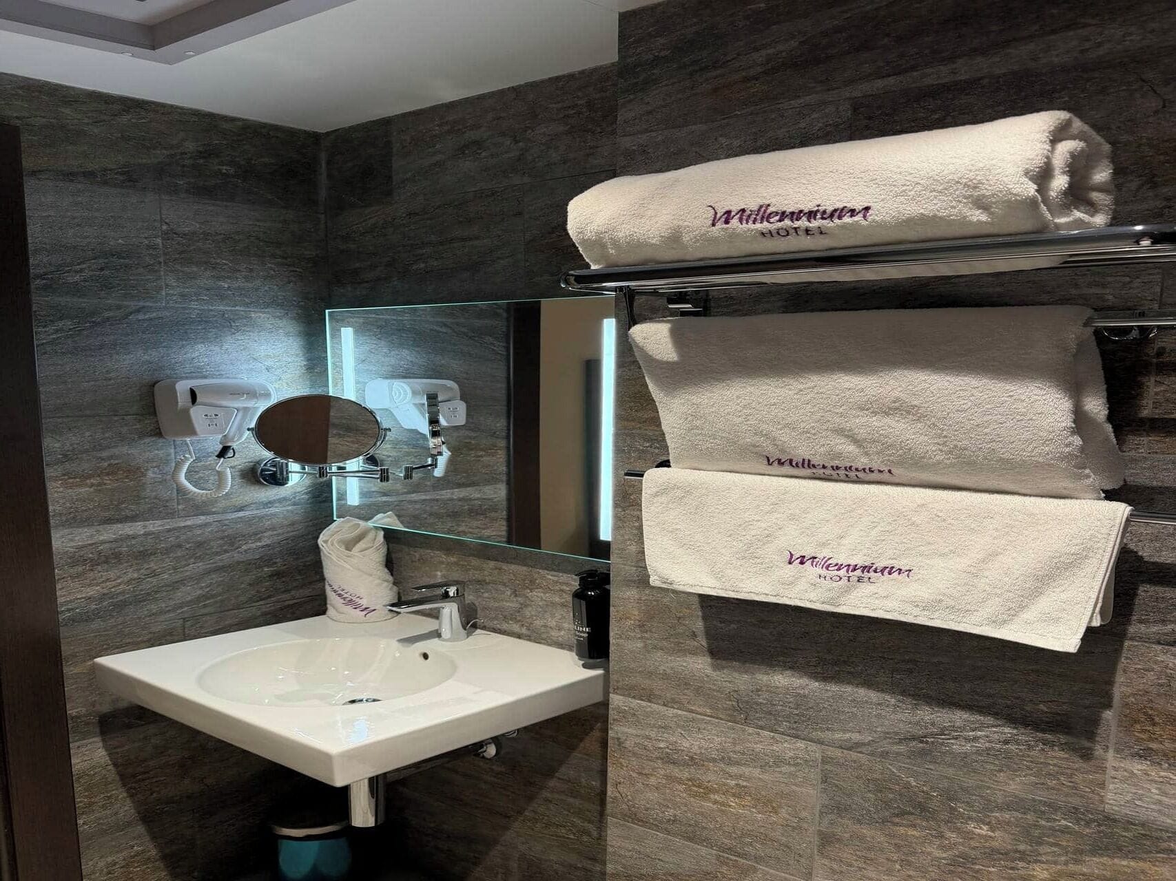 A bathroom with a sink, mirror, towel rack, and a hairdryer.