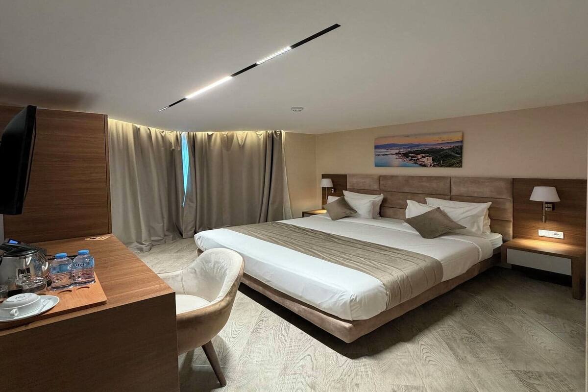 A hotel room with a bed, bedside tables, a desk with a chair, a TV, and a painting on the wall.