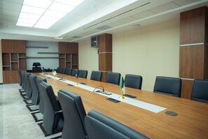 Un salón de conferencias con una larga mesa, sillas negras y una bandera.