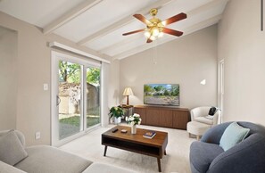 Uma sala de estar com ventilador de teto, mesa de centro, sofá, poltrona e televisão.