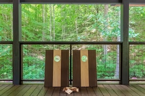 A room with a large window overlooking a forest, a wooden floor, and a pair of wooden doors with circular cutouts. - Rustic 2BR Farm Cabin: Hot Tub, Animals & Hiking (Sevierville)