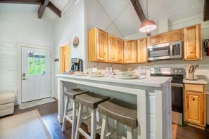 A kitchen with wooden cabinets, a microwave, an oven, and a bar stool seating area. - Rustic 2BR Farm Cabin: Hot Tub, Animals & Hiking (Sevierville)