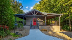 A cabin with a red door, a covered porch, and a gravel driveway. - Rustic 2BR Farm Cabin: Hot Tub, Animals & Hiking (Sevierville)