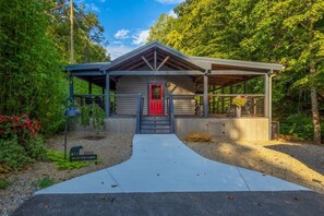 A cabin with a red door, a covered porch, and a gravel driveway. - Rustic 2BR Farm Cabin: Hot Tub, Animals & Hiking (Sevierville)